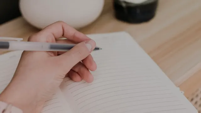 Ruka so zápisníkom a perom vedľa hrnčeka na drevenom stole