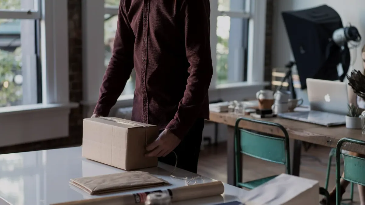 Muž balí kartónovú zásielku na stole v malom sklade e-shopu