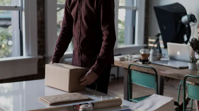 Muž balí kartónovú zásielku na stole v malom sklade e-shopu