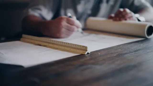 Projektant rysuje detail do výkresu pri rozloženom pauzovacom papieri s mierkou