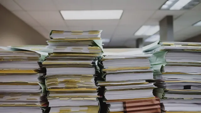 Vysoké stohy papierových zložiek a dokumentov na stole v kancelárii