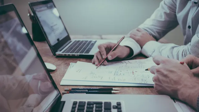 Ruky s perami nad plánom projektu medzi notebookmi