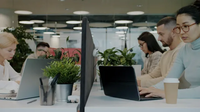 Rad kolegov pracuje na notebookoch pri stoloch vo veľkej otvorenej kancelárii